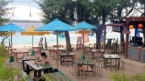 Un café frente a la playa con terraza y sombrillas, con vista al mar.