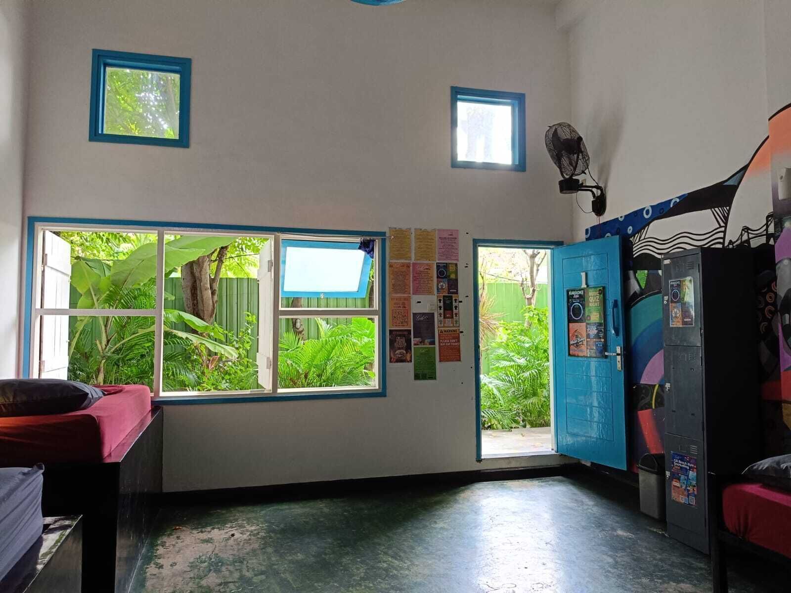 Une pièce avec une grande fenêtre, un lit, un bureau et une armoire bleue.