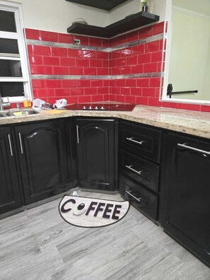 A kitchen with black cabinets, a red tiled backsplash, and a granite countertop. - Cozy 4-bedroom bungalow in Brevitor, St. Peter, where you can live like a local. (Mile and A Quarter)