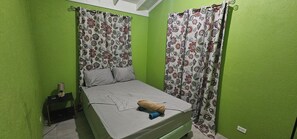 A small, single-bed room with green walls, floral curtains, and a bedside lamp. - Cozy 4-bedroom bungalow in Brevitor, St. Peter, where you can live like a local. (Mile and A Quarter)