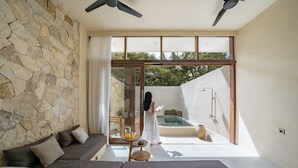 Una habitación moderna con pared de piedra, un gran ventanal corredero que da a una zona de piscina y un espacio de estar con sofás y una mesa.