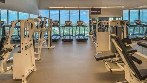 Un gimnasio con cintas de correr, máquinas de pesas y grandes ventanales que ofrecen vistas a la ciudad.