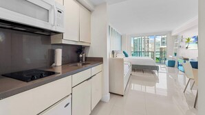 A modern kitchen with a built-in microwave, a black induction cooktop, and white cabinetry. - ARYA Luxury Adjoining Suites Ocean View (Miami)