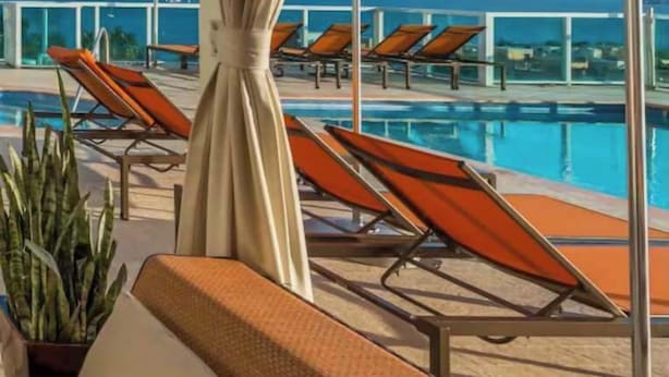 A poolside area with lounge chairs and umbrellas, overlooking a clear blue sky and a distant view of the sea. - ARYA Luxury Adjoining Suites Ocean View (Miami)