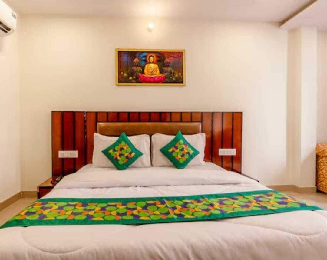 Ein Hotelzimmer mit einem Holz-Kopfteil, einem Bett mit weißen Leinen, zwei grün gemusterten Kissen und einer farbenfrohen Tagesdecke.
