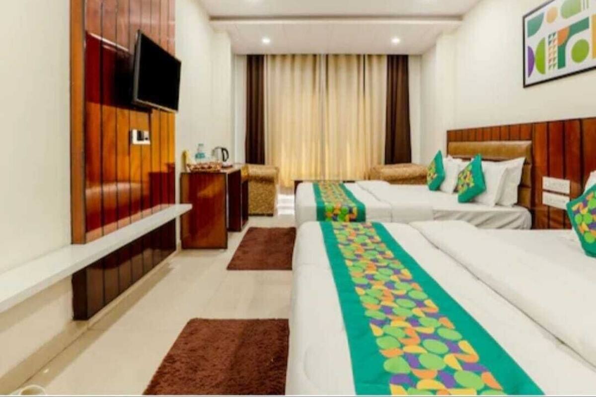 Ein Hotelzimmer mit zwei Betten, einem an einer Holzvertäfelung montierten Fernseher, einem Deckenventilator und einem Fenster mit Vorhängen.