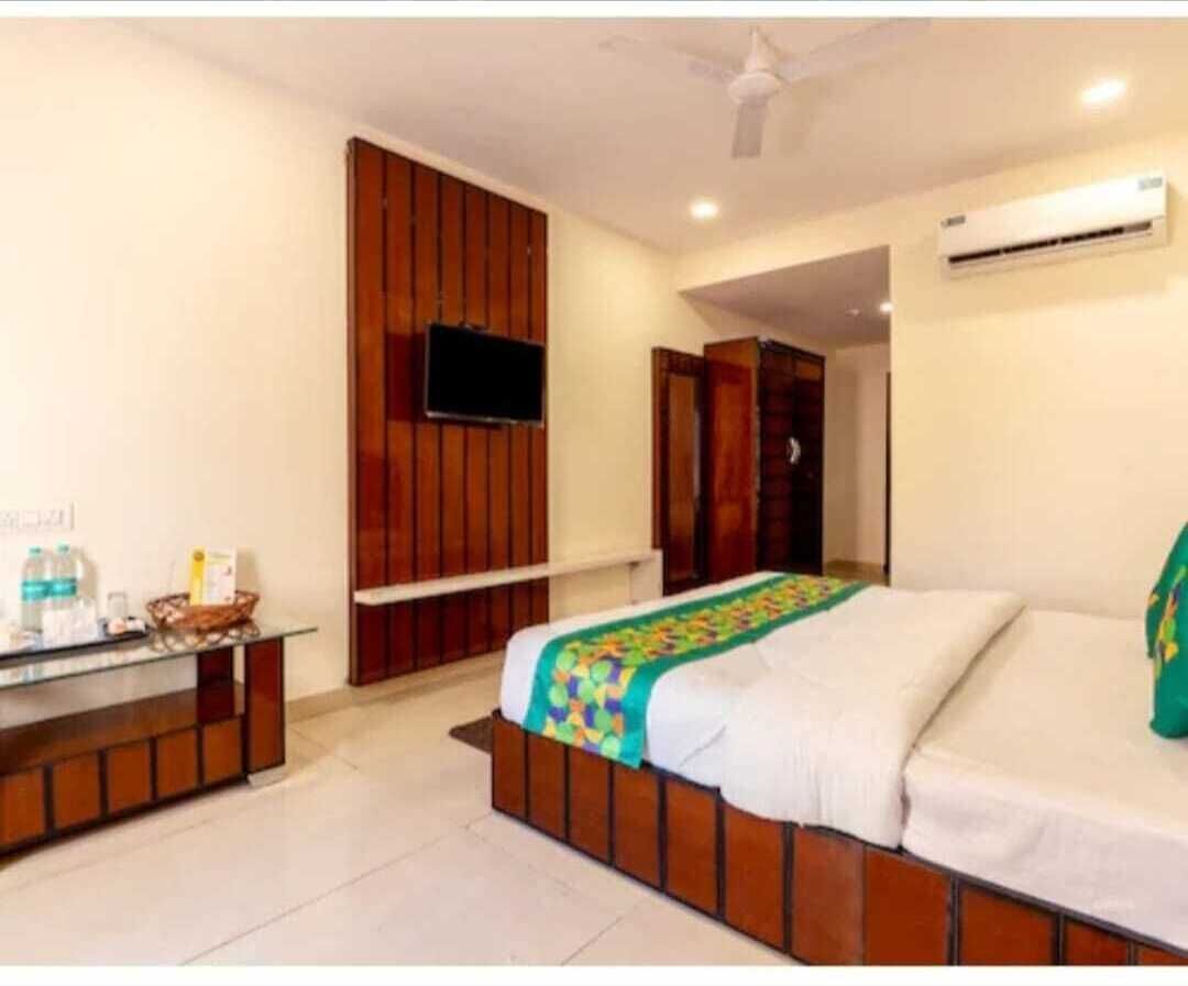 A hotel room with a bed, a TV mounted on the wall, a desk with a chair, and an air conditioning unit.
