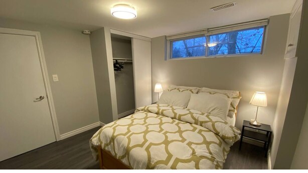 Ein Schlafzimmer mit einem Bett, zwei Nachttischlampen, einem Fenster mit Blick auf Bäume und einem Kleiderschrank.