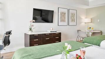 Habitación de hotel con dos camas, televisión, obras de arte enmarcadas, escritorio y alfombra verde.