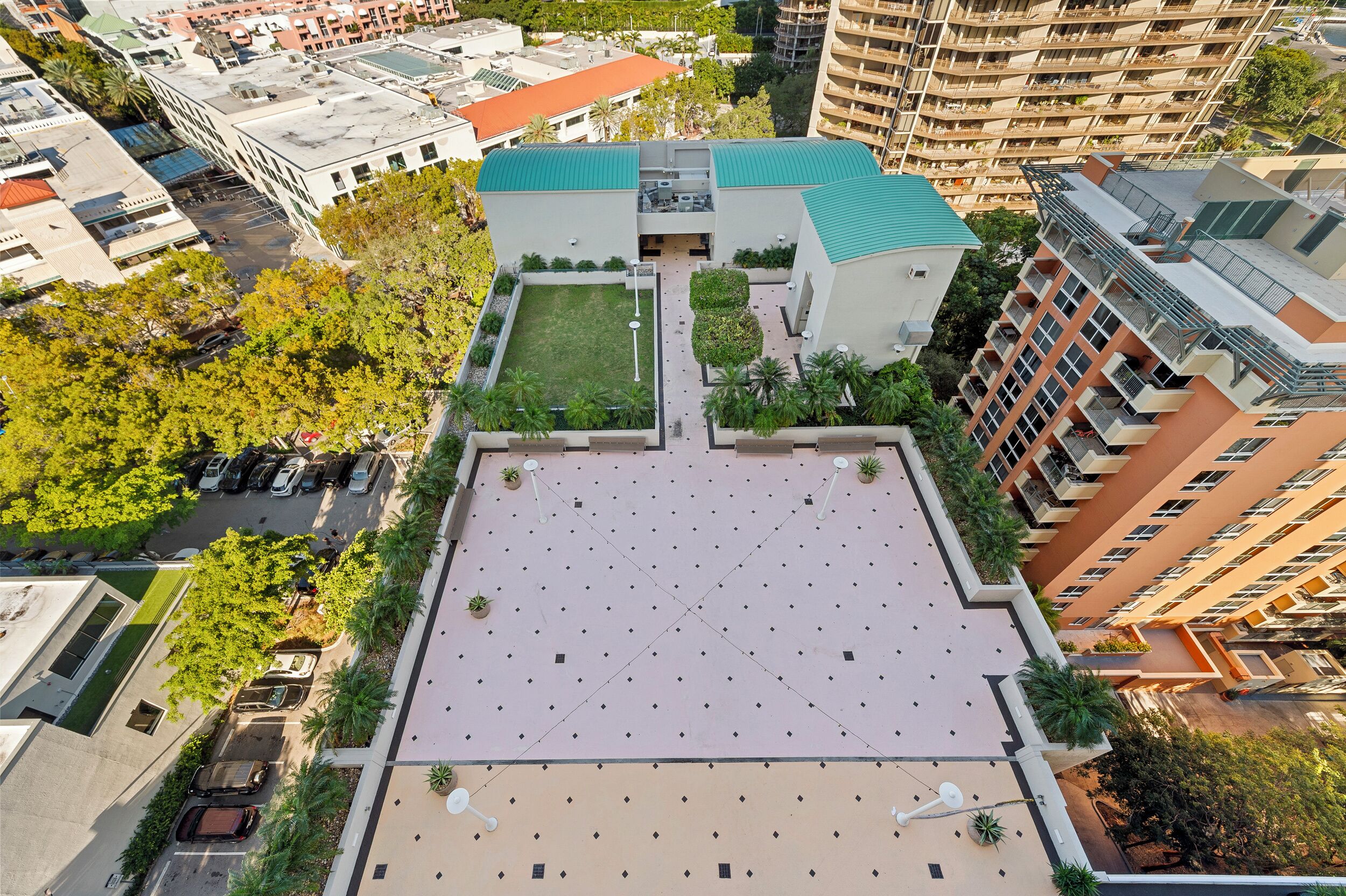 Vue aérienne d’un bâtiment moderne doté d’une terrasse sur le toit, entouré d’arbres et d’autres immeubles.