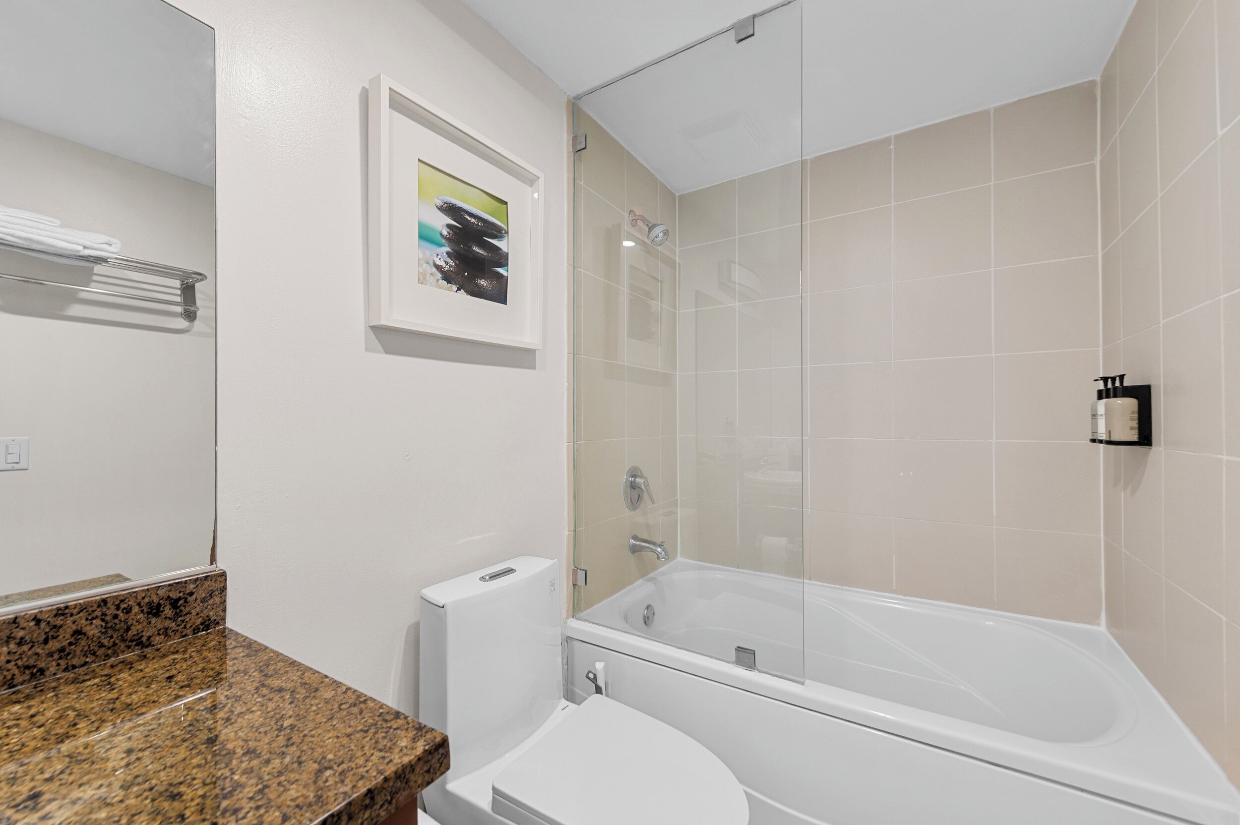 A modern bathroom with a white toilet, a granite countertop, a bathtub, and a glass shower enclosure.