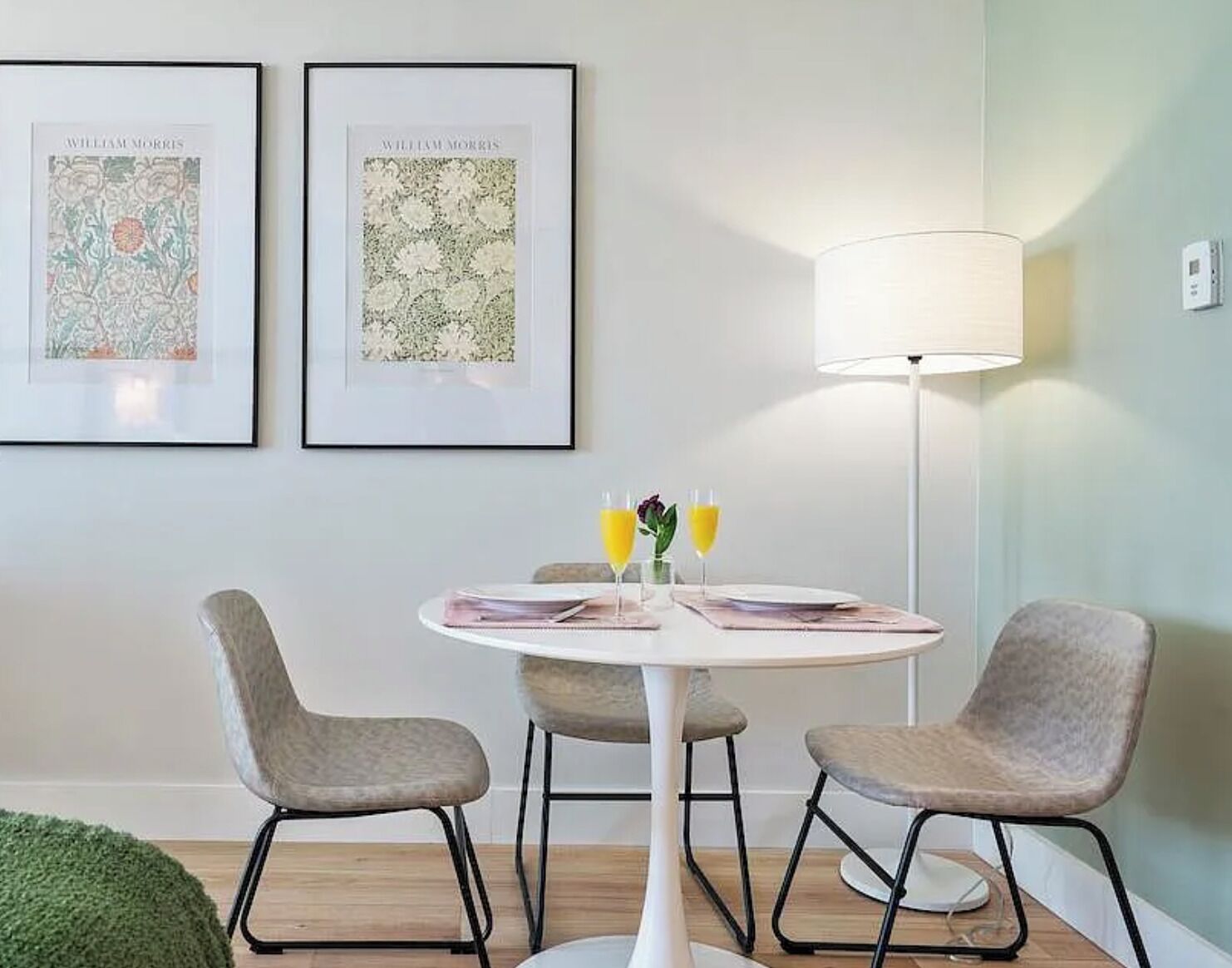 A room with a round table, two chairs, a lamp, and two framed pictures on the wall.