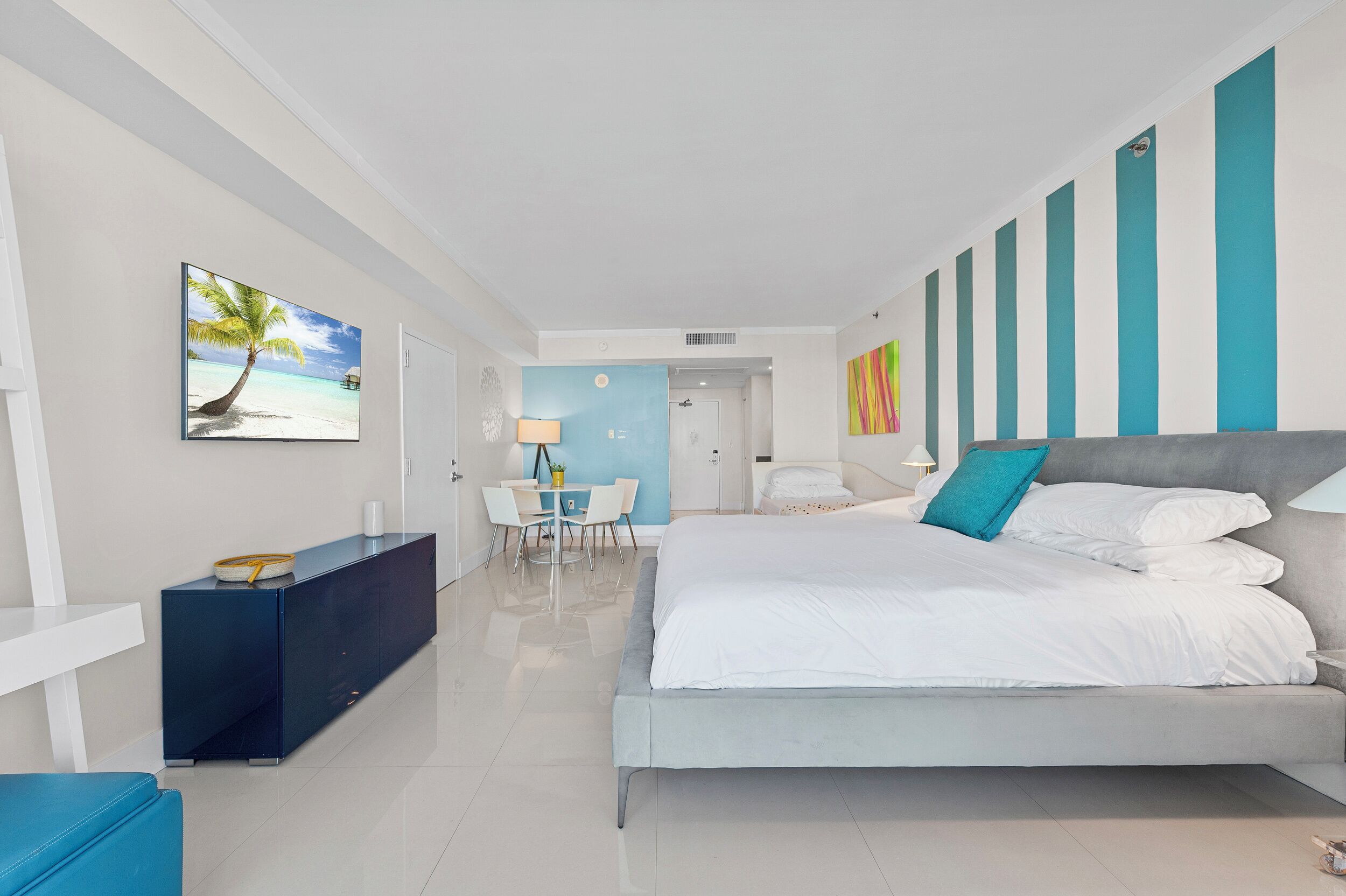 Habitación de hotel moderna con una cama grande, un escritorio y una silla. En la pared, hay un cuadro de una playa.