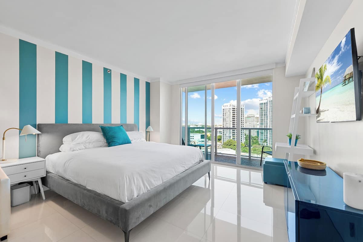 Habitación de hotel moderna con una cama grande, un escritorio y vistas de la ciudad a través de ventanales del suelo al techo.