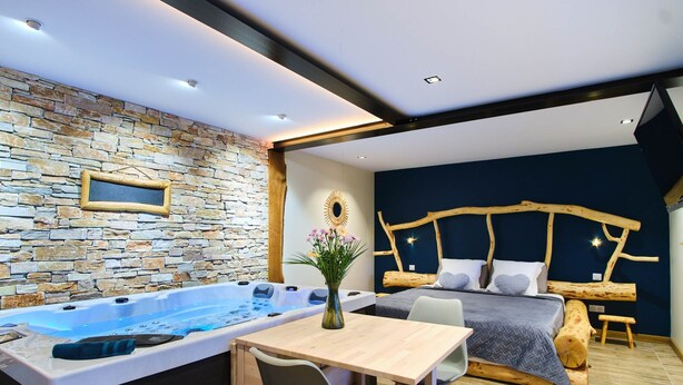 Un dormitorio moderno con pared de piedra, cabecero de madera, cama grande, mesa de madera y bañera de hidromasaje.