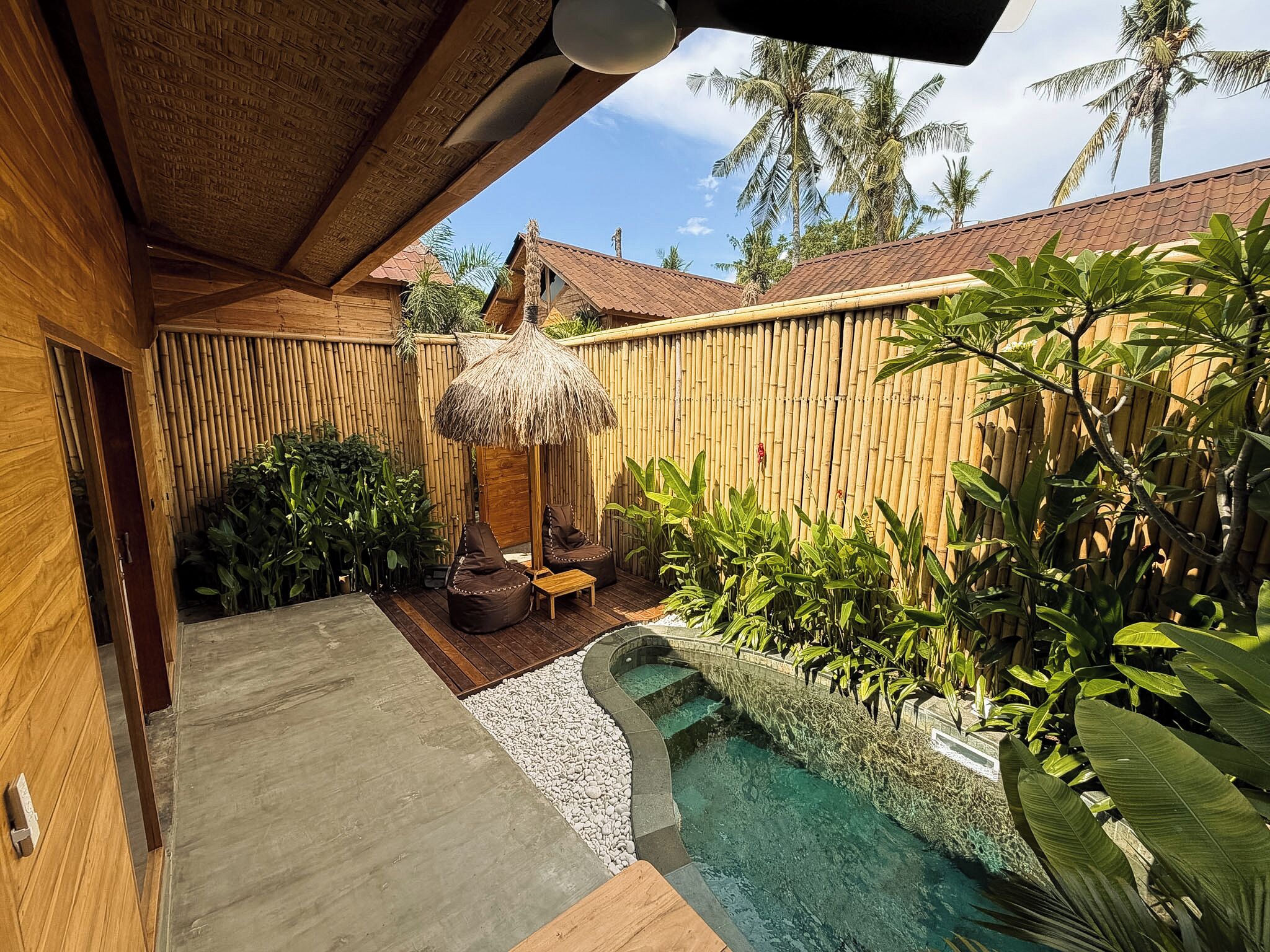 A wooden house with a thatched roof, a small pool, and lush tropical plants.