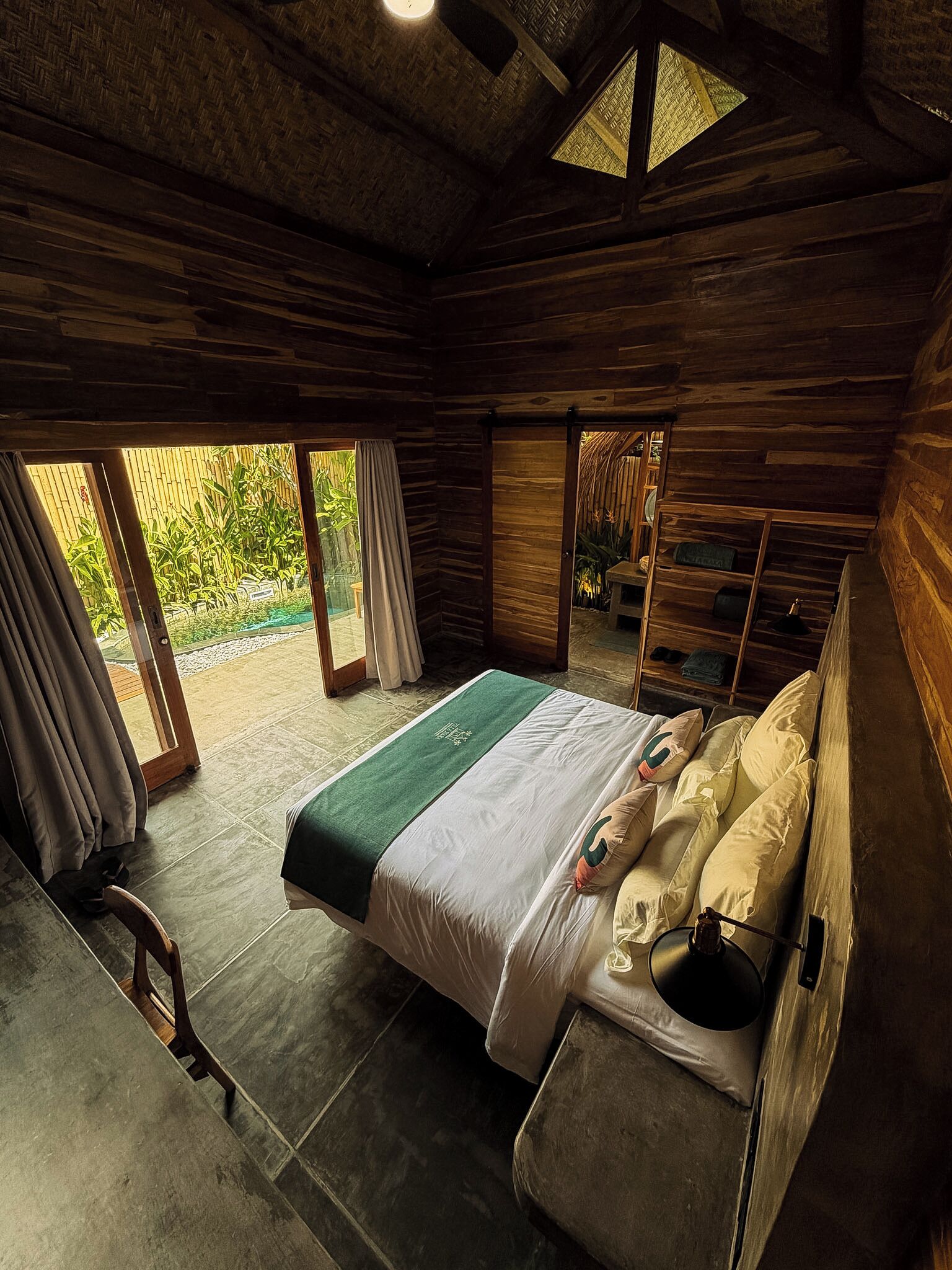 Een houten kamer met een bed, een klein tafeltje en uitzicht op groen.