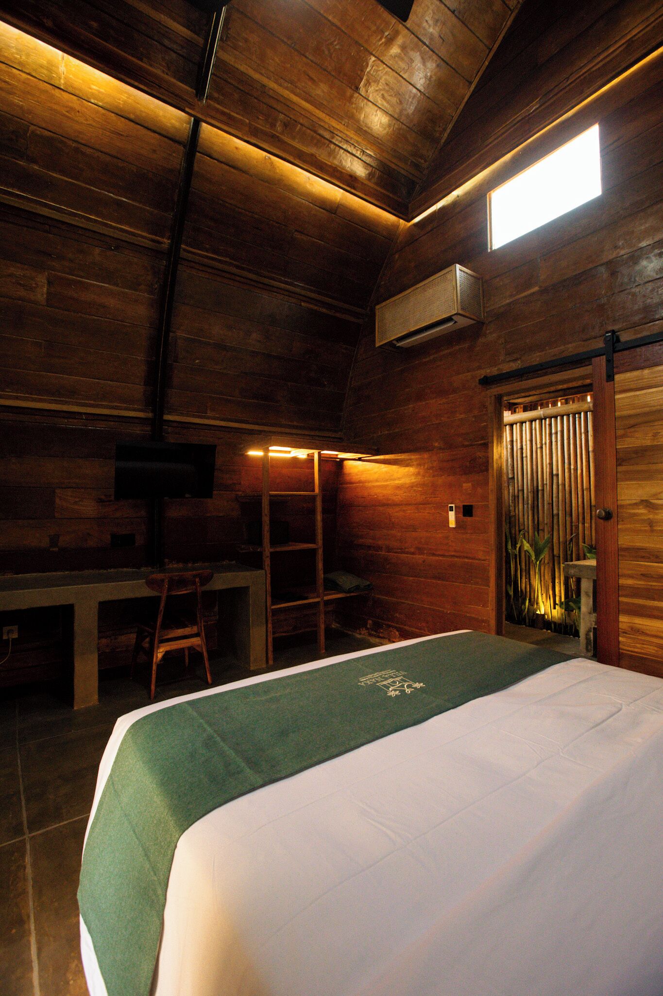 A wooden room with a bed, a desk, a chair, and a television.