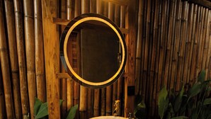 Un baño con lavamanos de piedra, tocador de madera y un espejo con marco circular.