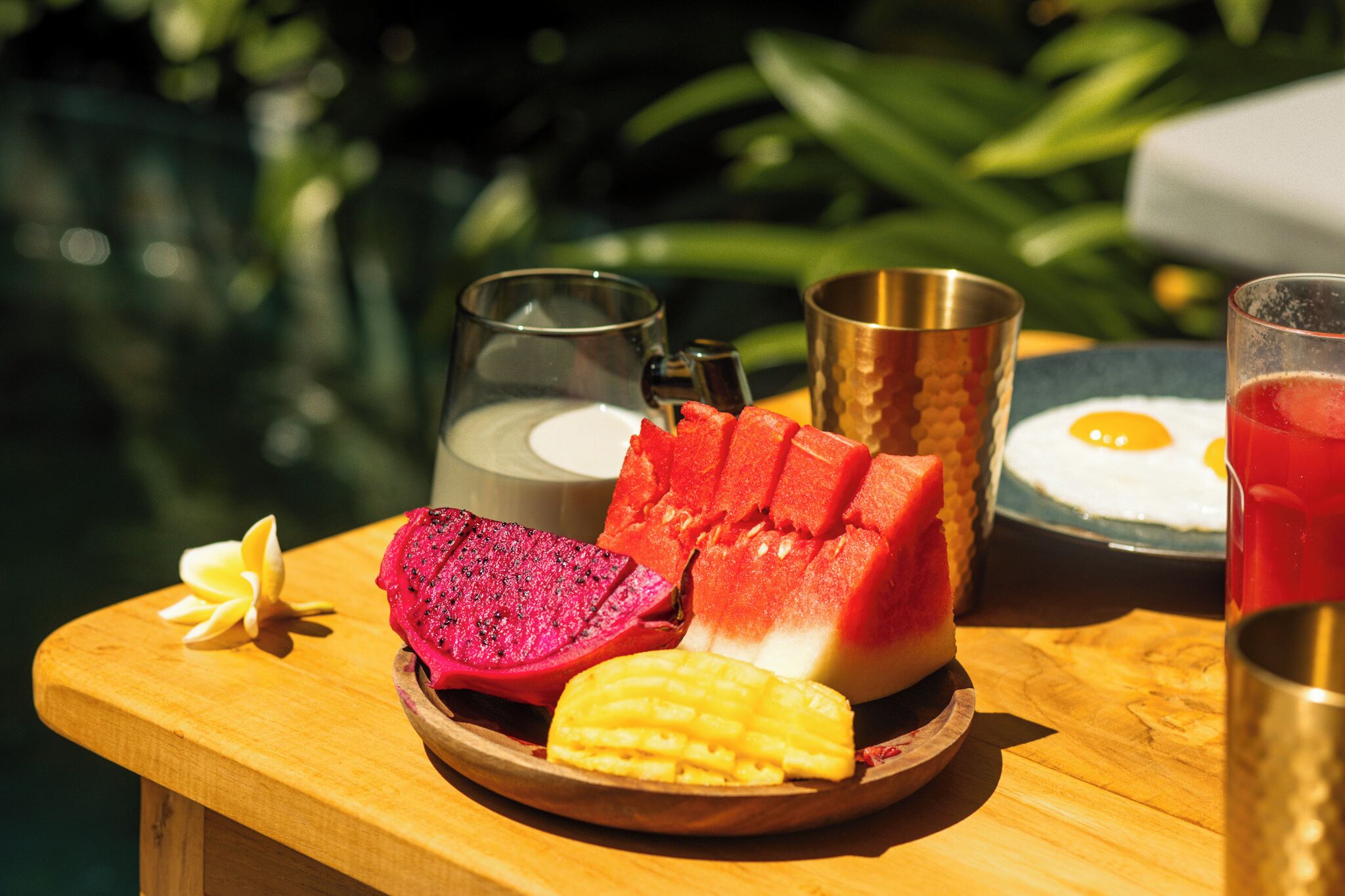 A wooden table with a plate of fruit, a glass of milk, and a glass of red drink.