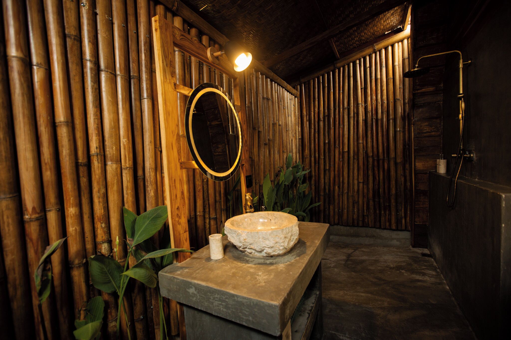 A bathroom with a stone sink, bamboo wall, and a shower area.