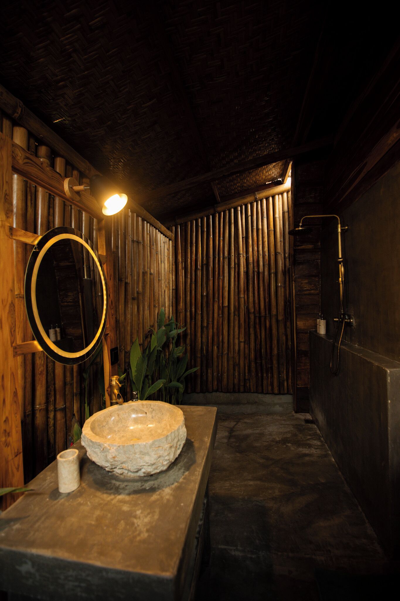 Un baño con un lavabo de piedra, pared de madera y un espejo redondo.