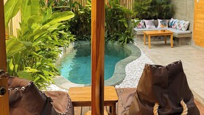 Zona de piscina con techo de paja, sillas de descanso y plantas tropicales.