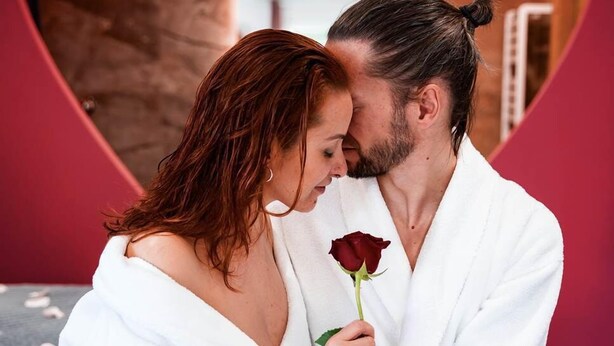 A couple in white bathrobes sitting on a bed with a heart-shaped mirror in the background. - Loft Bisous Sucré - Romantic Suite & Private Jacuzzi (CARSPACH)