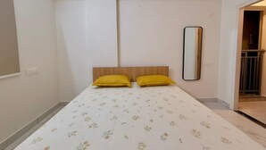 Ein Schlafzimmer mit einem Bett, zwei Kissen, einem Holzkopfende, einem Spiegel und einer blumengemusterten Bettdecke.
