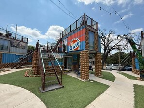 A building with a Gulf logo, a staircase, and a fenced area with artificial grass. - KBPPE Rooftop View@InnHabit—Family & Couples Slp 8 (Medicine Park)