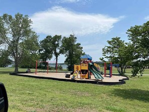 A playground with a slide, swings, and a climbing structure. - KBPPE Rooftop View@InnHabit—Family & Couples Slp 8 (Medicine Park)