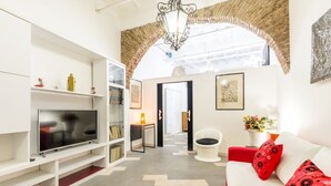 Un salon moderne avec un téléviseur à écran plat, un canapé blanc, des coussins rouges et un lustre.