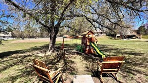 Un parque infantil con un tobogán, columpios y dos sillas de madera.