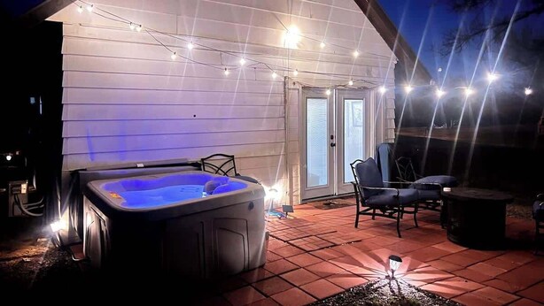 Un jacuzzi bajo un porche cubierto con guirnaldas de luces, una silla y una mesa.