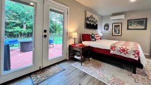 Un dormitorio con cama, mesita de noche, lámpara, ventana y aire acondicionado.
