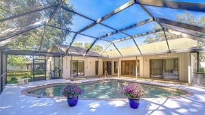A covered outdoor swimming pool with a glass enclosure, surrounded by potted plants, and a house in the background. - Spacious 4-bedroom house in quaint Tampa with AC (Tampa)