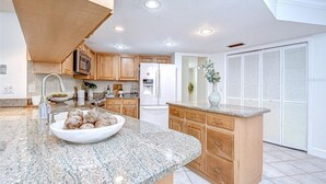 A modern kitchen with granite countertops, wooden cabinets, a built-in microwave, and a refrigerator. - Spacious 4-bedroom house in quaint Tampa with AC (Tampa)