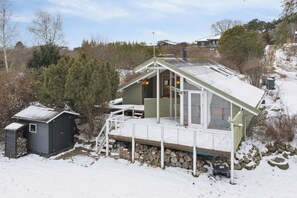 Une petite cabane à un seul étage, dotée d’un porche, d’un petit abri de jardin et de fondations en pierre.