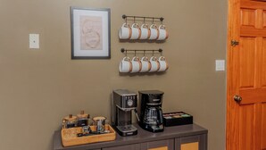 En kaffestation med kaffemaskine, kopper og en kurv med ting på en bordplade.