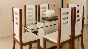 Un'area pranzo con un tavolo in vetro circondato da sedie di legno con schienali traforati. Sul tavolo è posata una composizione floreale, e un lampadario pende dal soffitto.