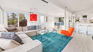Un moderno salón con una mesa baja de vidrio, un sofá con cojines estampados y un sillón naranja brillante.