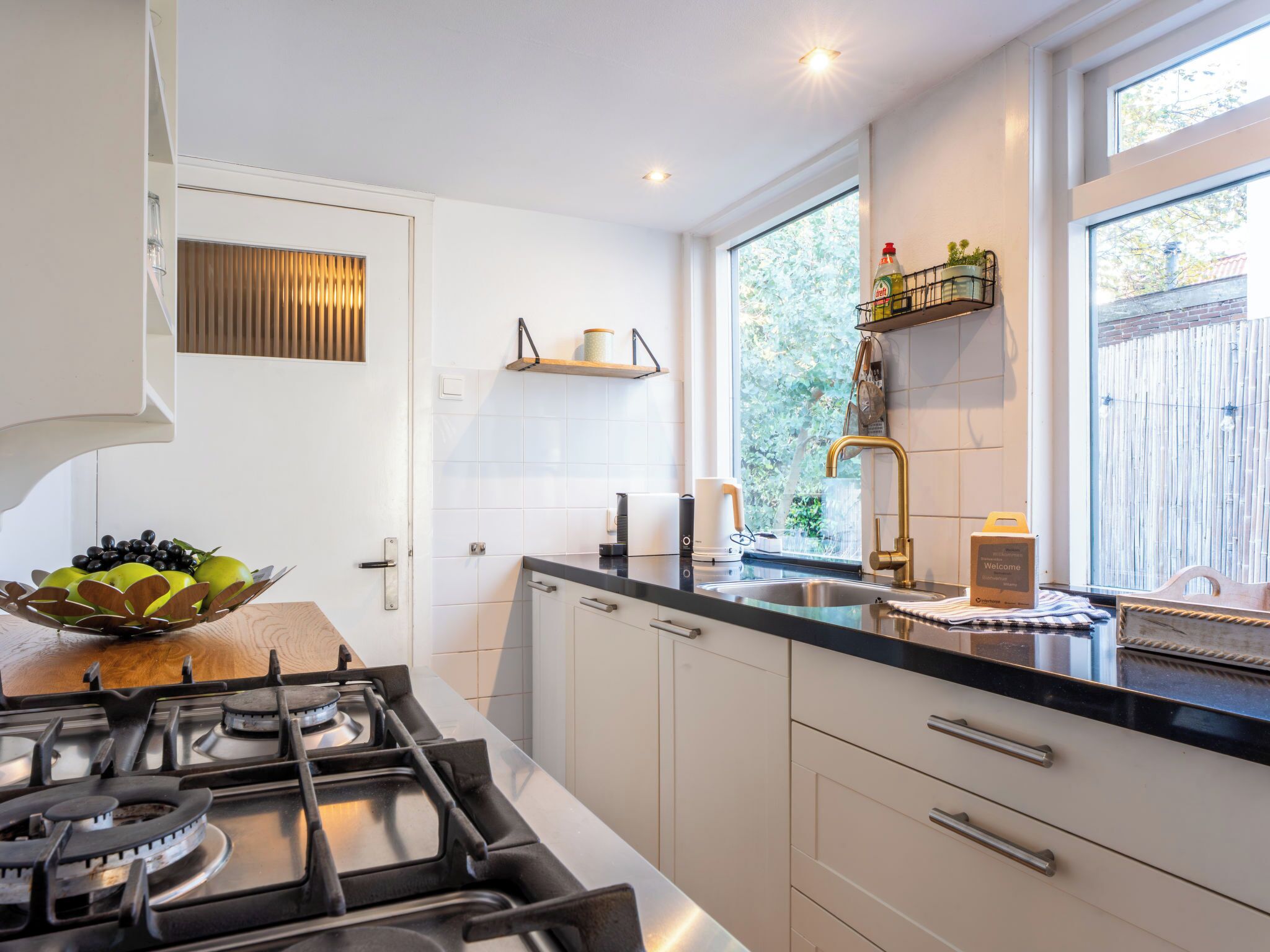 A modern kitchen with a gas stove, white cabinets, and a window with a view of greenery.