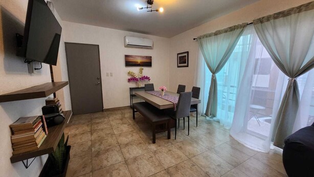 Una sala de estar con una mesa de comedor, sillas, un televisor y una estantería.