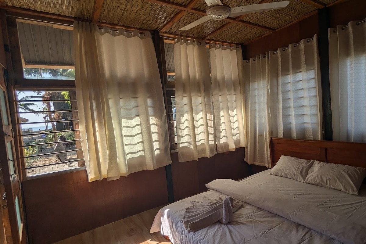Una habitación con cama, ventilador de techo y ventana con cortinas.