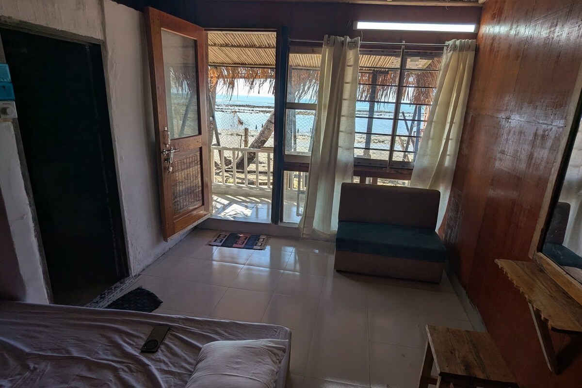 Una habitación con una cama, un banco, una mesita y vistas a la playa a través de un ventanal grande.