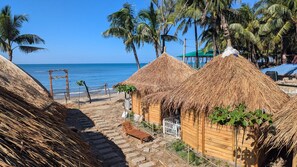 Thatched-roof huts with a beach view, wooden benches, and a clear sky. - Beach Valley Eco Resort Saint Martin (Saint Martin's Island)