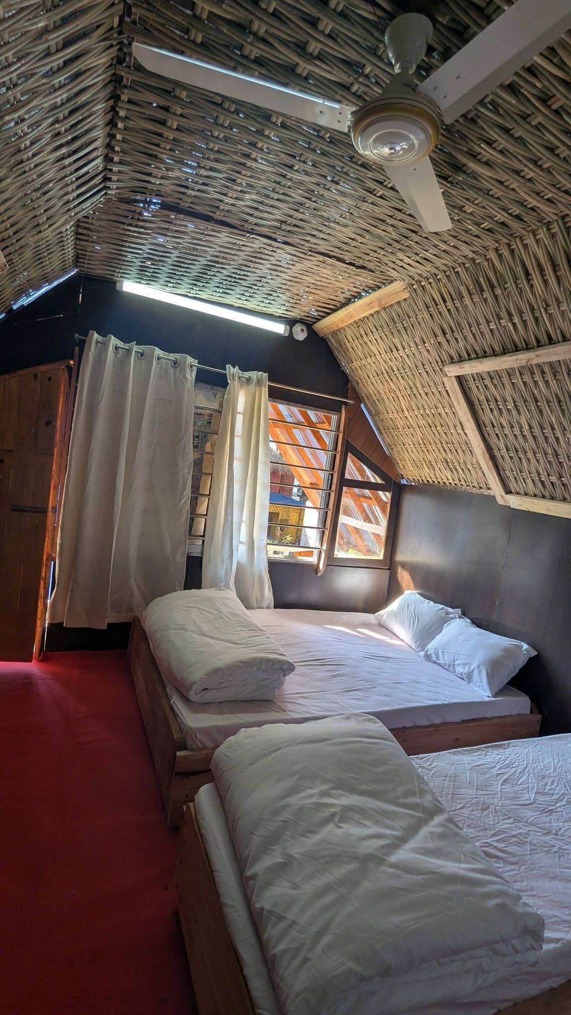 A room with two beds, a ceiling fan, and a window with curtains.