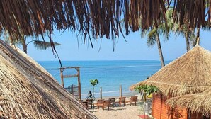 A beach view from a room with a thatched roof, wooden furniture, and a view of the ocean. - Beach Valley Eco Resort Saint Martin (Saint Martin's Island)