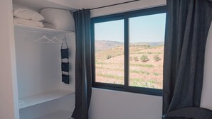 Quarto com uma janela ampla, uma cama, uma cadeira e um guarda-roupa cheio de roupas.