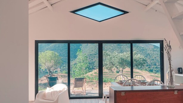 Interior moderno com uma grande porta de vidro deslizante que dá para um terraço ao ar livre, uma mesa de jantar de madeira e uma cadeira branca.